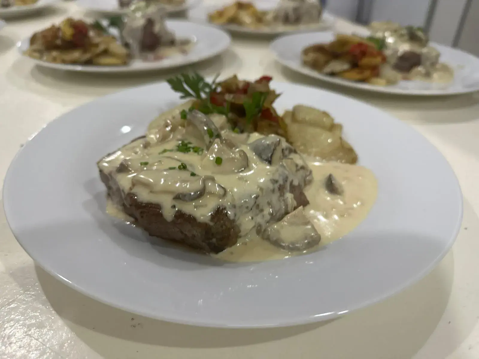 Plato de bife con salsa de crema y hongos, acompañado de papas