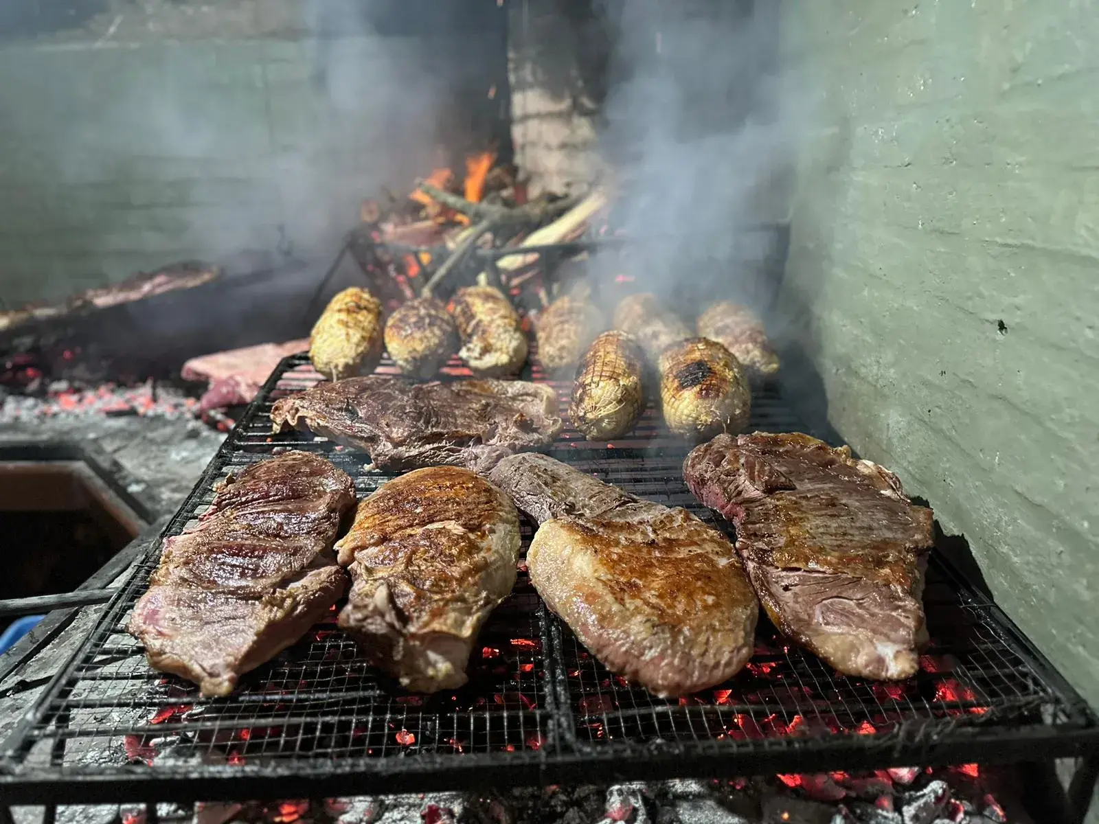Bifes y choclos asándose sobre la parrilla, con brasas encendidas y humo